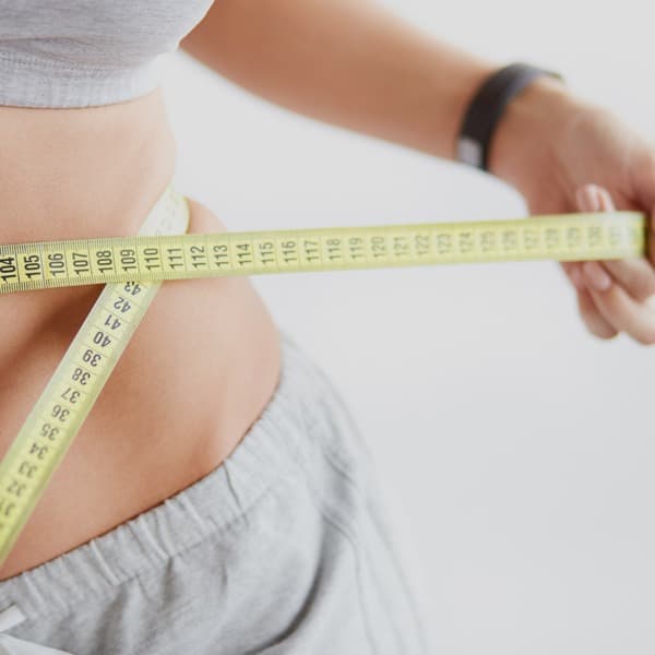Image d'une femme mesurant son tour de taille illustrant la perte de graisse par le froid par cryolipolyse