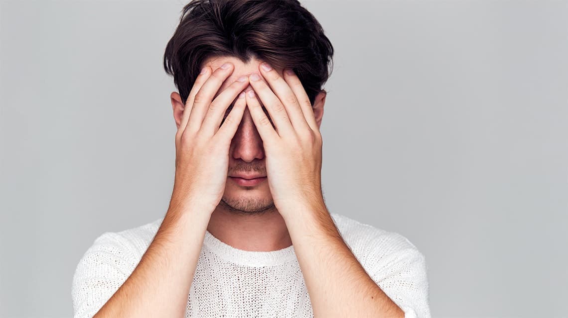 Un homme se cache le visage pour illustrer le complexe fréquent à cause de l'acné chez l'adulte
