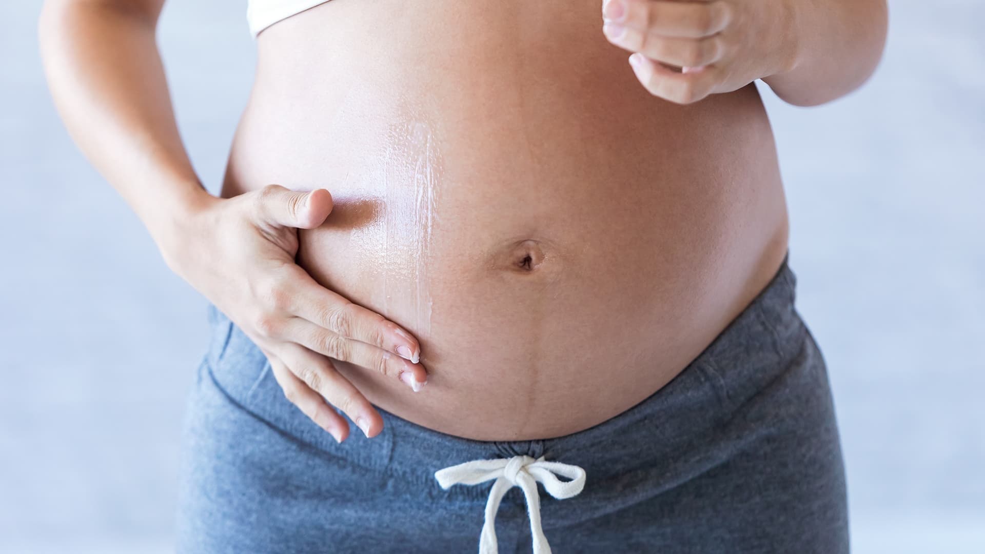 Une femme enceinte s'applique une crème préventive contre les vergetures sur le ventre