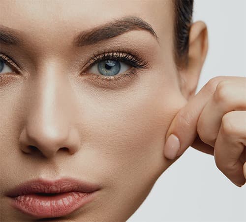 Une femme se tire la peau de la joue pour mimer les effets d'injection d'inducteur tissulaire sur les rides